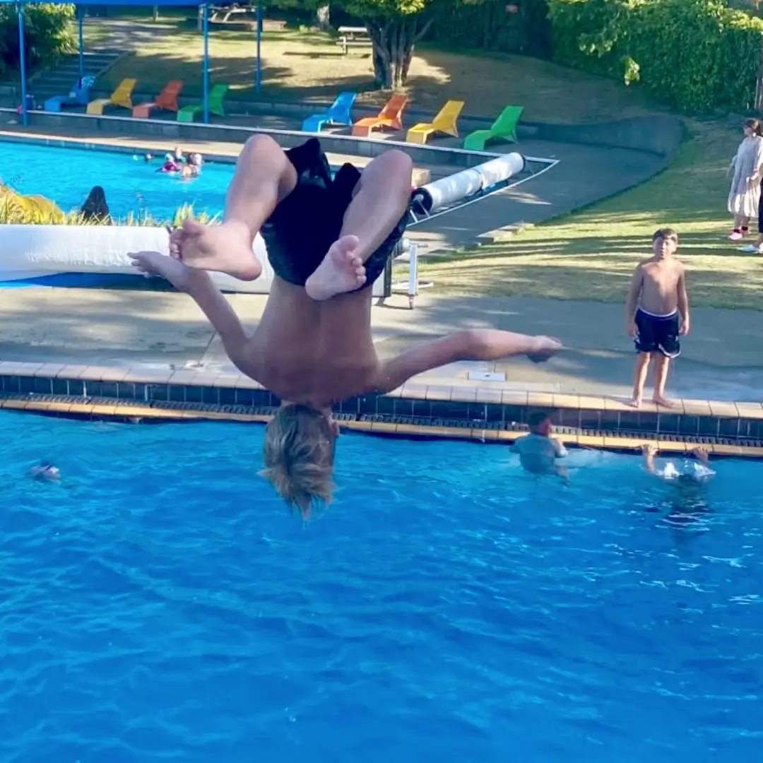 A youth is performing a flip, about to land headfirst into a swimming pool